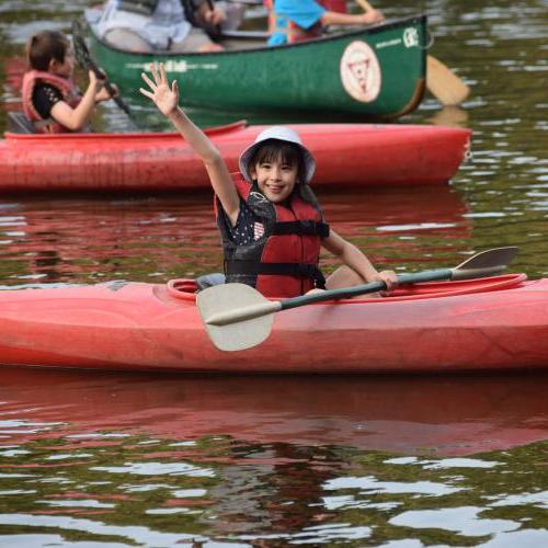 一个女孩在马萨索伊特湖参加夏令营时从她的皮艇上挥手. 